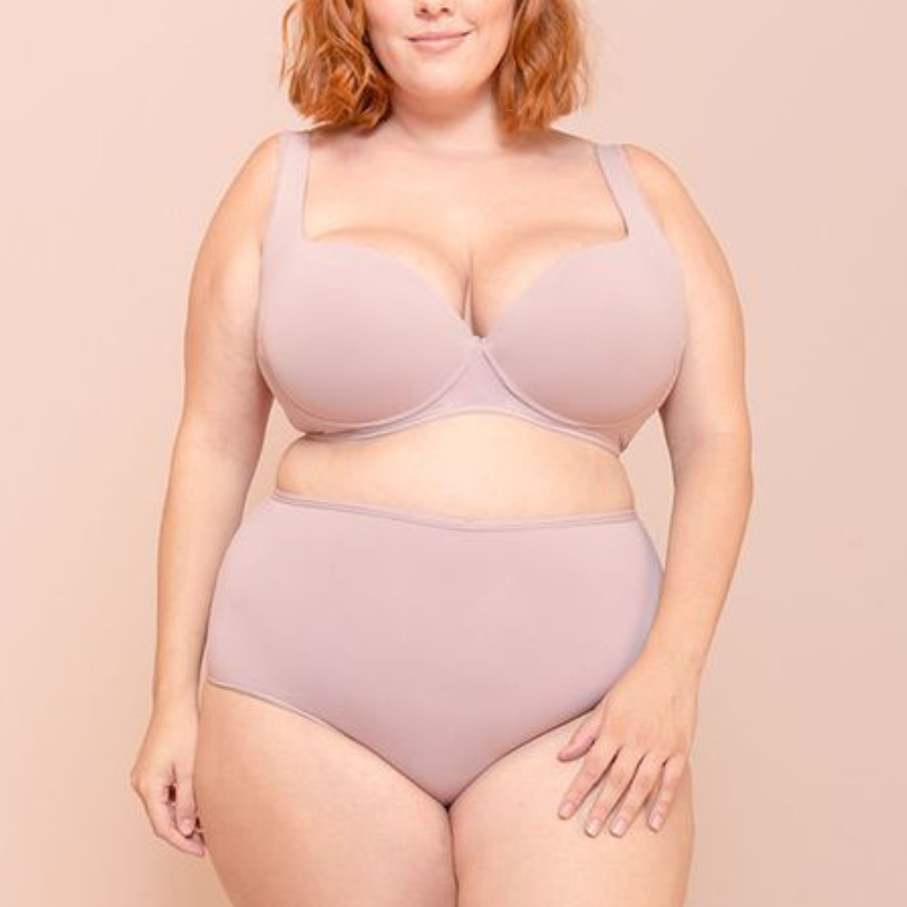 Mulher plus size vestindo conjunto de lingerie nude com sustentação, representando conforto, confiança e valorização do corpo real.