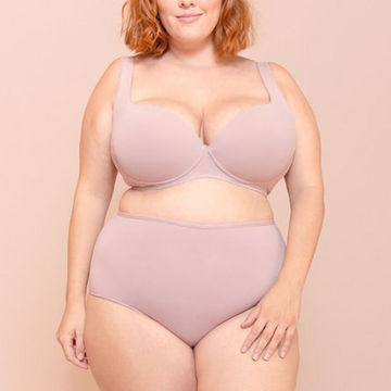 Mulher plus size vestindo conjunto de lingerie nude com sustentação, representando conforto, confiança e valorização do corpo real.
