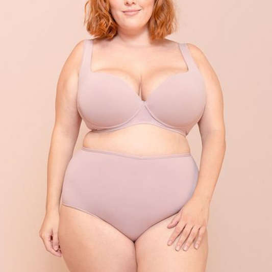 Mulher plus size vestindo conjunto de lingerie nude com sustentação, representando conforto, confiança e valorização do corpo real.