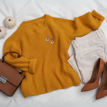 Look outonal com suéter mostarda de tricô, calça off-white de sarja, sapato caramelo de salto, bolsa marrom e brincos dourados sobre fundo branco.