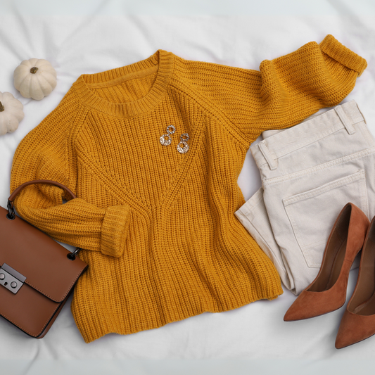 Look outonal com suéter mostarda de tricô, calça off-white de sarja, sapato caramelo de salto, bolsa marrom e brincos dourados sobre fundo branco.