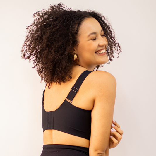 Mulher sorridente de costas usando sutiã preto com alças largas, expressando conforto, liberdade e autoestima.