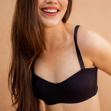 Mulher sorrindo, vestindo sutiã preto com alças ajustáveis, transmitindo leveza, conforto e autoestima com lingerie básica e funcional.