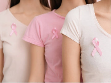 Mulheres usando camisetas em tons de rosa e branco com laços do Outubro Rosa presos no peito, simbolizando a conscientização sobre o câncer de mama.