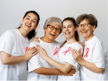 Grupo de mulheres de diferentes idades sorrindo e abraçadas, usando camisetas brancas com o laço rosa do Outubro Rosa, simbolizando união e conscientização sobre a prevenção do câncer de mama.