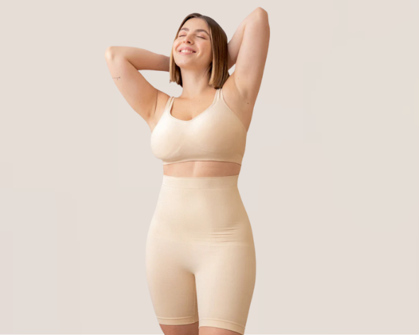 Mulher sorridente usando conjunto de lingerie modeladora bege, com top e short de cintura alta, em pose descontraída e confiante.