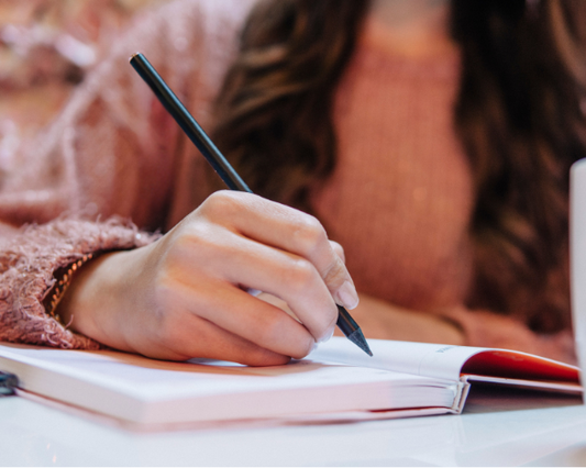 Mulher escrevendo em um caderno em ambiente tranquilo, simbolizando revisão e planejamento de metas pessoais.