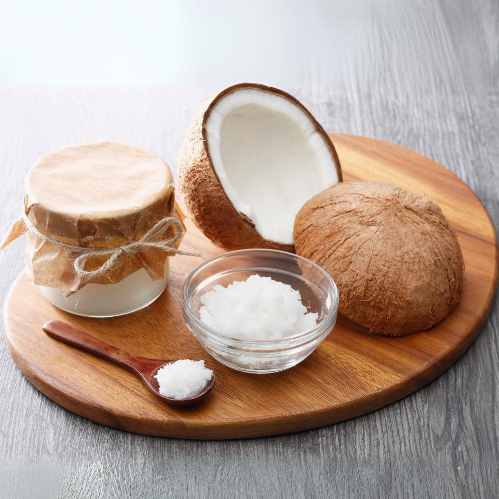 Pote e colher com óleo de coco ao lado de coco fresco sobre tábua de madeira, representando o uso natural do ingrediente na beleza e cuidados pessoais.