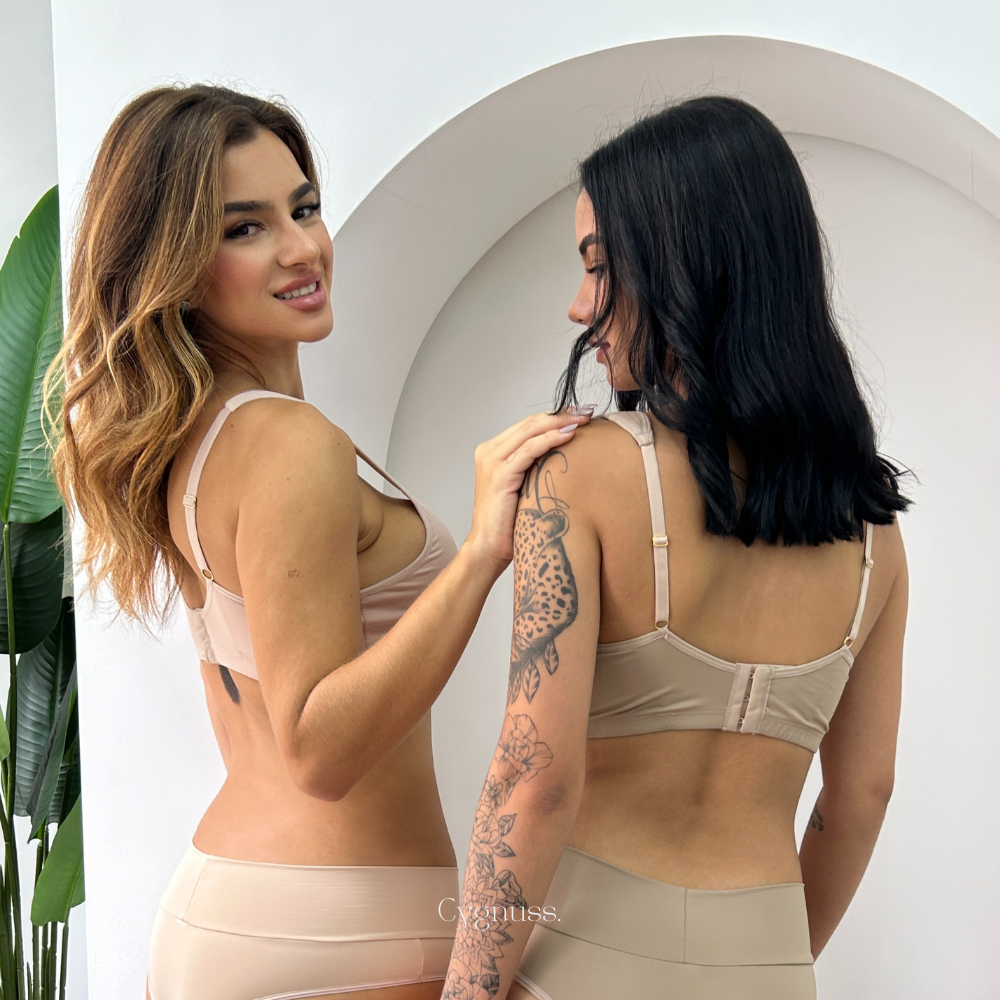 Duas mulheres vestindo lingerie Cygnuss bege, exibindo o design das costas e o caimento da tanga Calcinha Pandora.