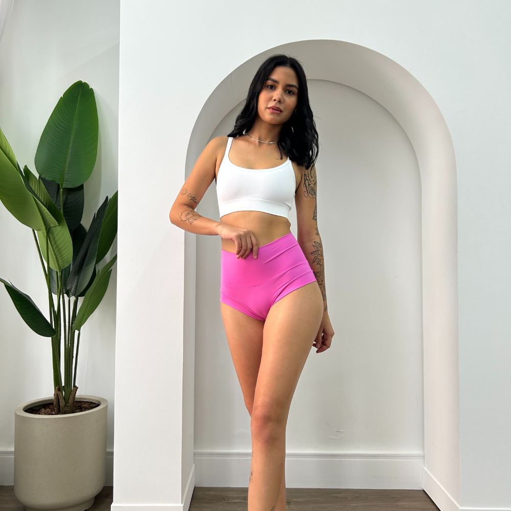 Mulher modelando shortinho Calcinha Névoa com cintura alta na cor rosa, oferecendo sustentação abdominal e conforto.
