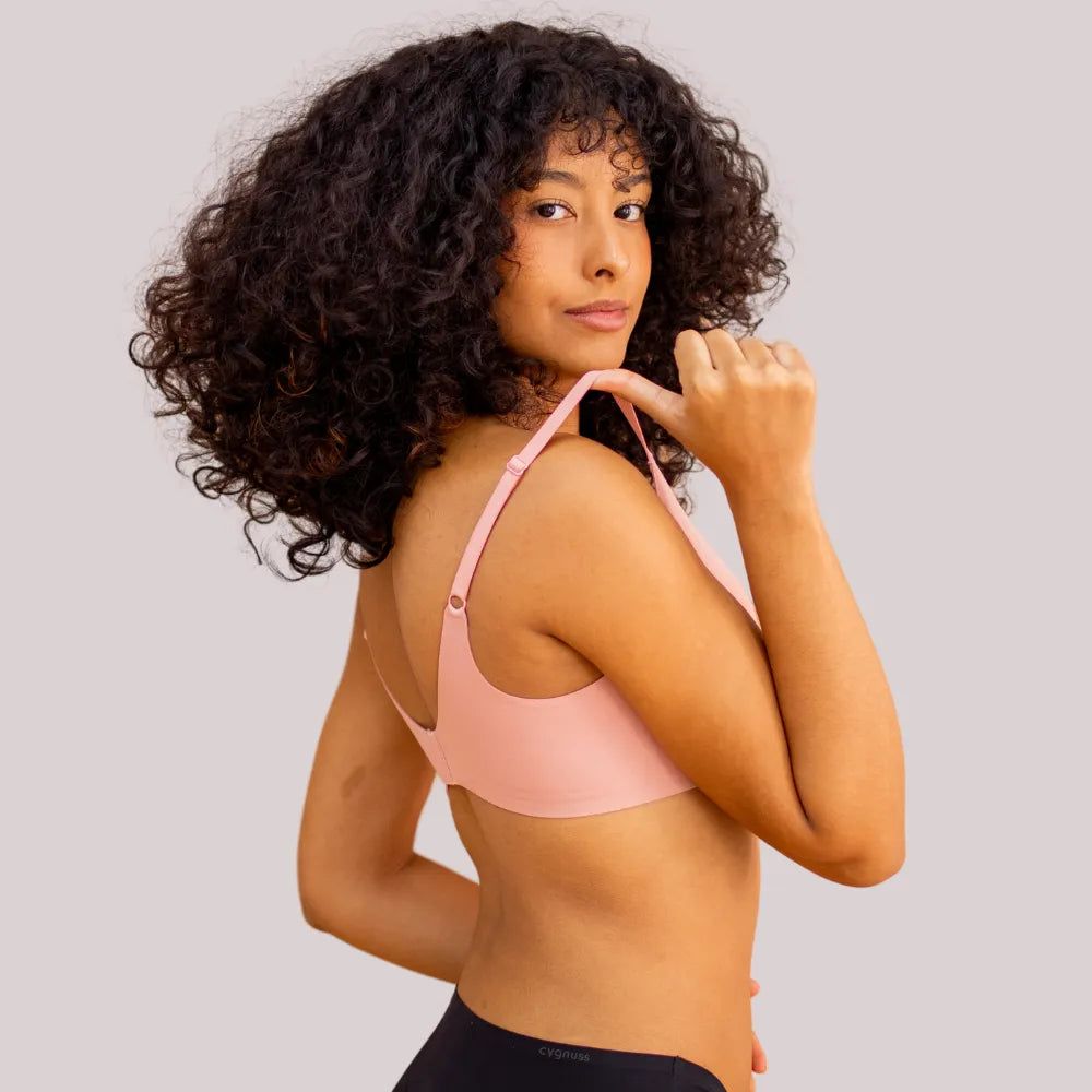 Mulher de cabelos cacheados vestindo o Sutiã Alça Fina Cygnuss na cor rose, segurando a alça ajustável para demonstrar a elasticidade e conforto.