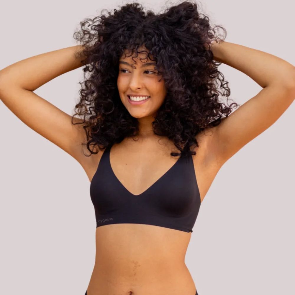 Modelo de cabelos cacheados sorrindo enquanto veste o Sutiã Alça Fina Cygnuss na cor preta, demonstrando o ajuste confortável e toque macio da peça.