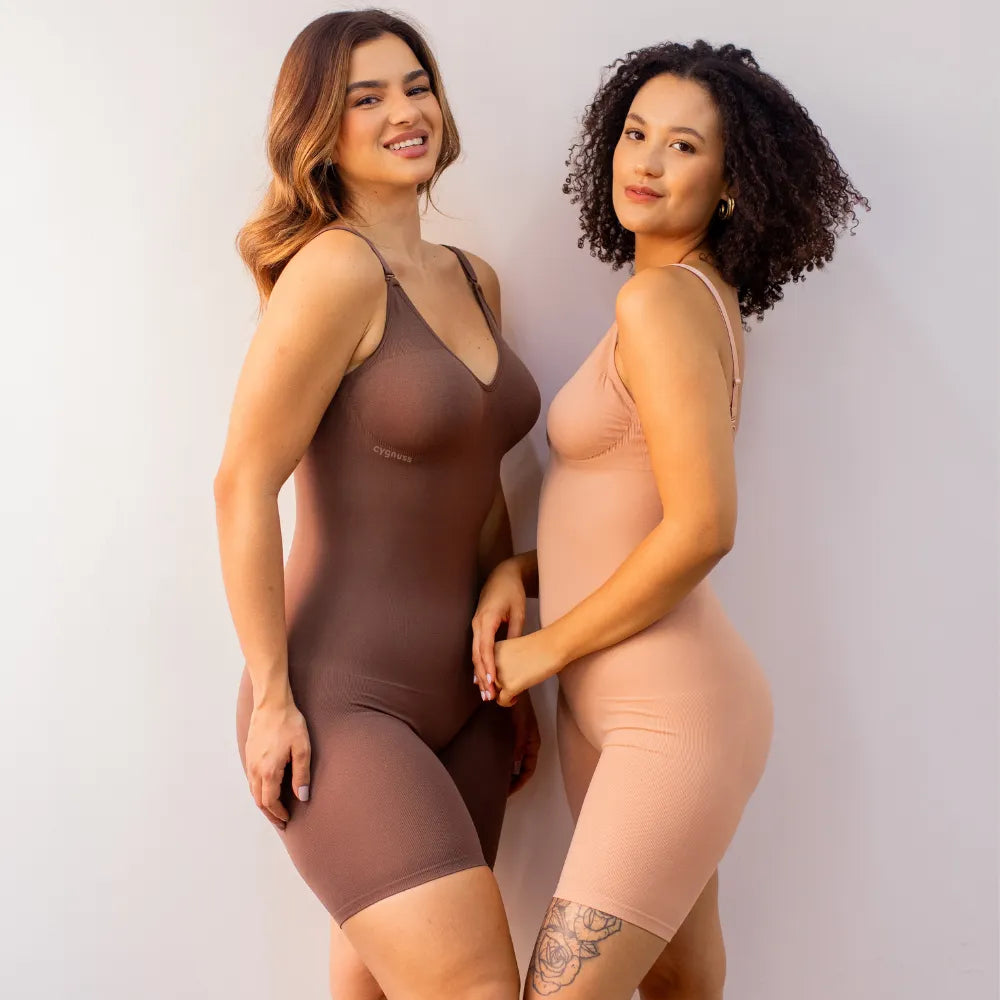 Duas mulheres usando o Body Elegance Modelador em tom marrom e tom pele. Ambas estão sorrindo e exibindo o ajuste perfeito e elegante dos bodies, com o logo da Cygnuss visível no canto superior esquerdo de ambas as peças.