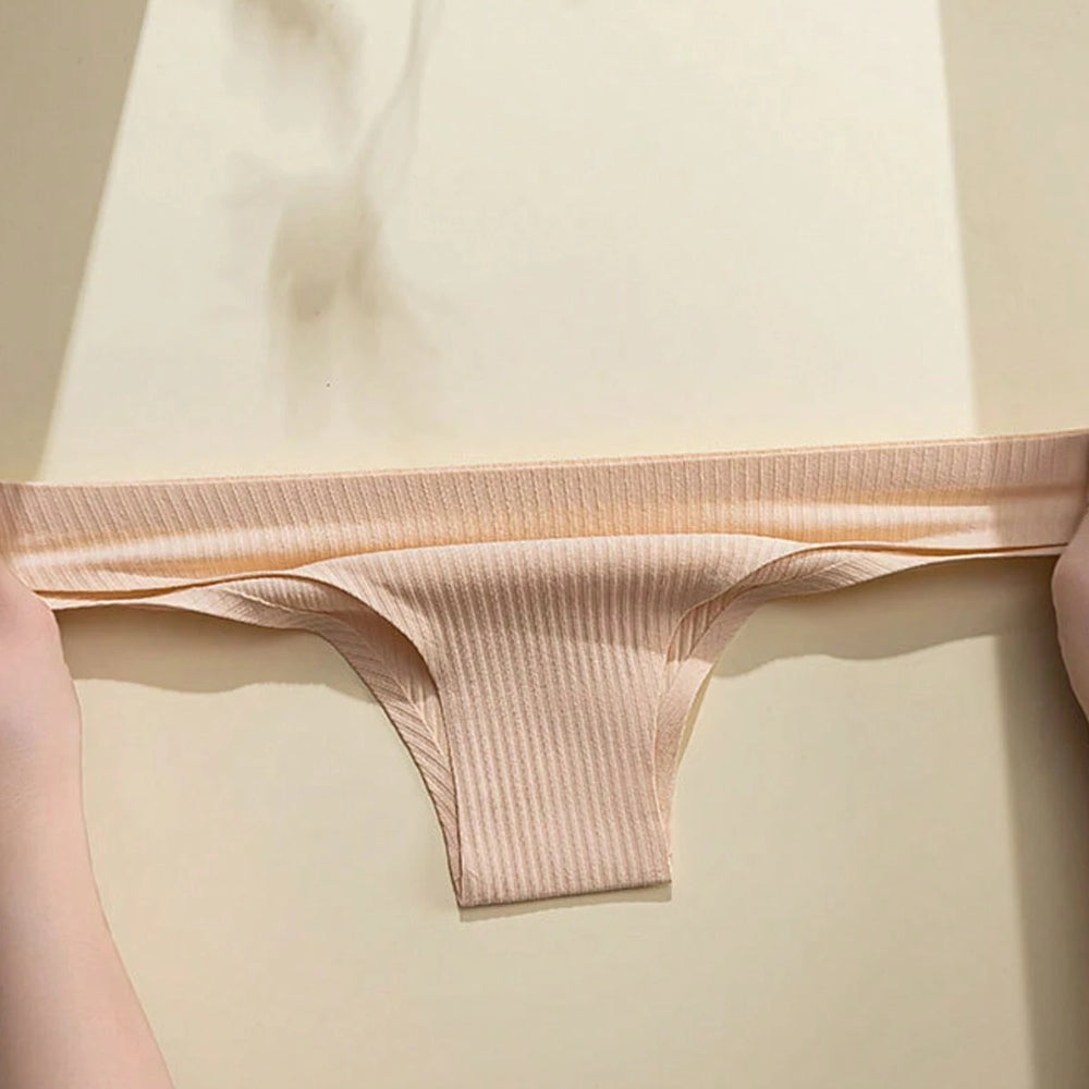 Imagem mostra uma calcinha canelada na cor bege sendo esticada por duas mãos, evidenciando a elasticidade e a suavidade do tecido com elastano. A iluminação suave destaca a textura em relevo do material.