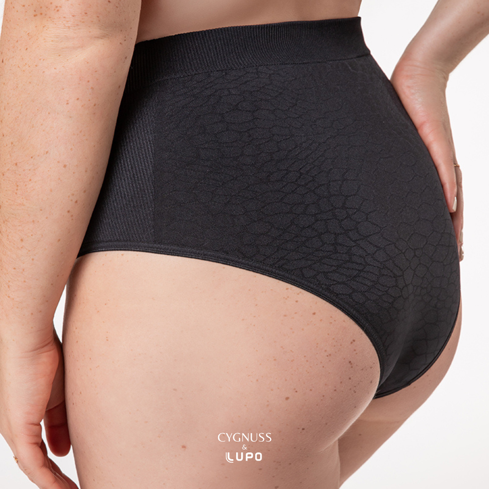 Close-up lateral de uma mulher usando uma calcinha modeladora preta de cintura alta. O tecido texturizado sem costuras apresenta um design elegante, com áreas estratégicas de compressão suave para modelar a silhueta. A cintura elástica garante ajuste confortável, enquanto o material respirável proporciona frescor ao longo do dia. O logotipo da Cygnuss & Lupo está sobreposto na parte inferior da peça.