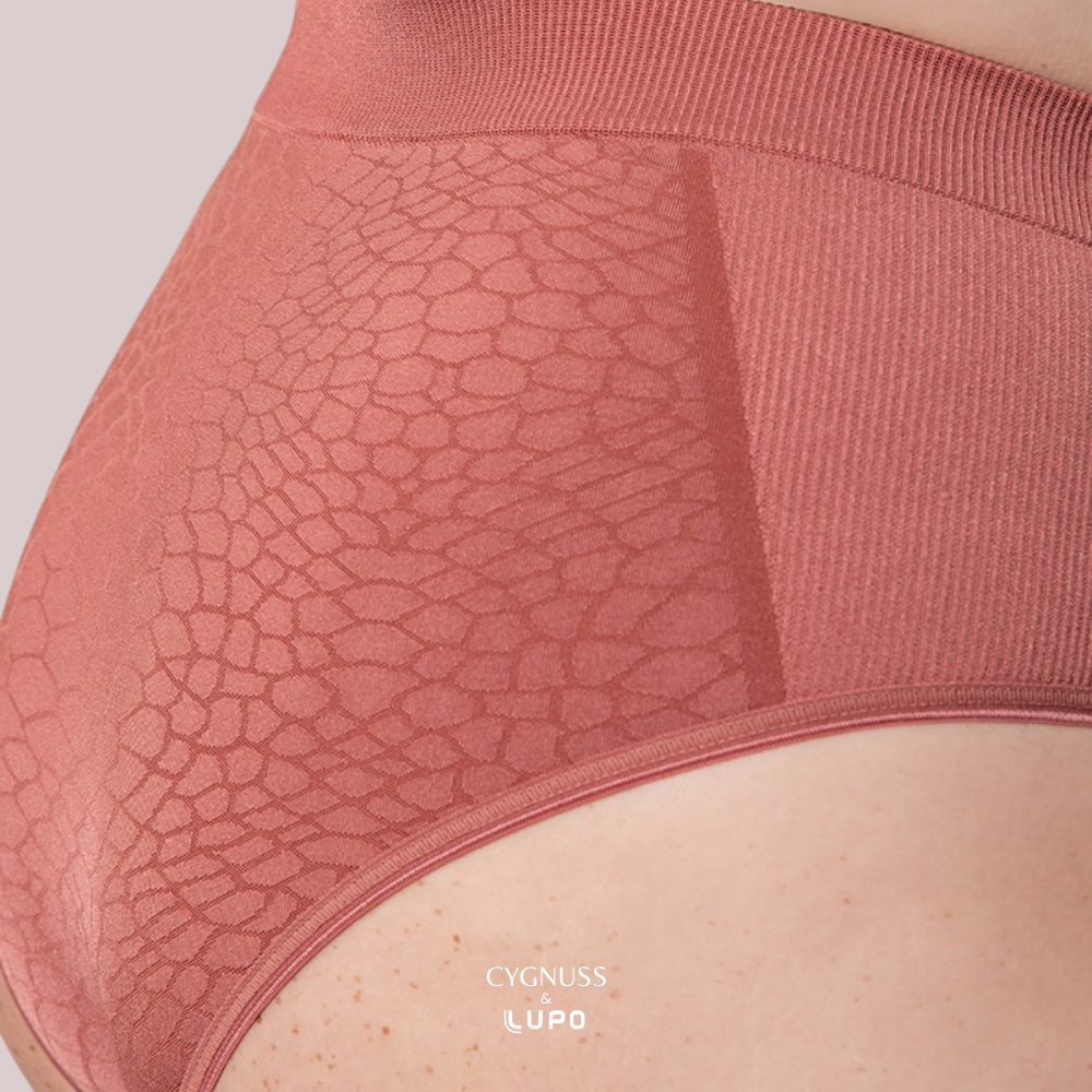 Close-up lateral de uma mulher usando uma calcinha modeladora de cintura alta na cor telha. O tecido possui um padrão texturizado elegante e sem costuras, oferecendo compressão moderada e conforto. A modelagem firme ajusta-se ao corpo, proporcionando definição e sustentação. O logotipo da Cygnuss & Lupo está sobreposto na parte inferior da peça. Fundo nude rosado.