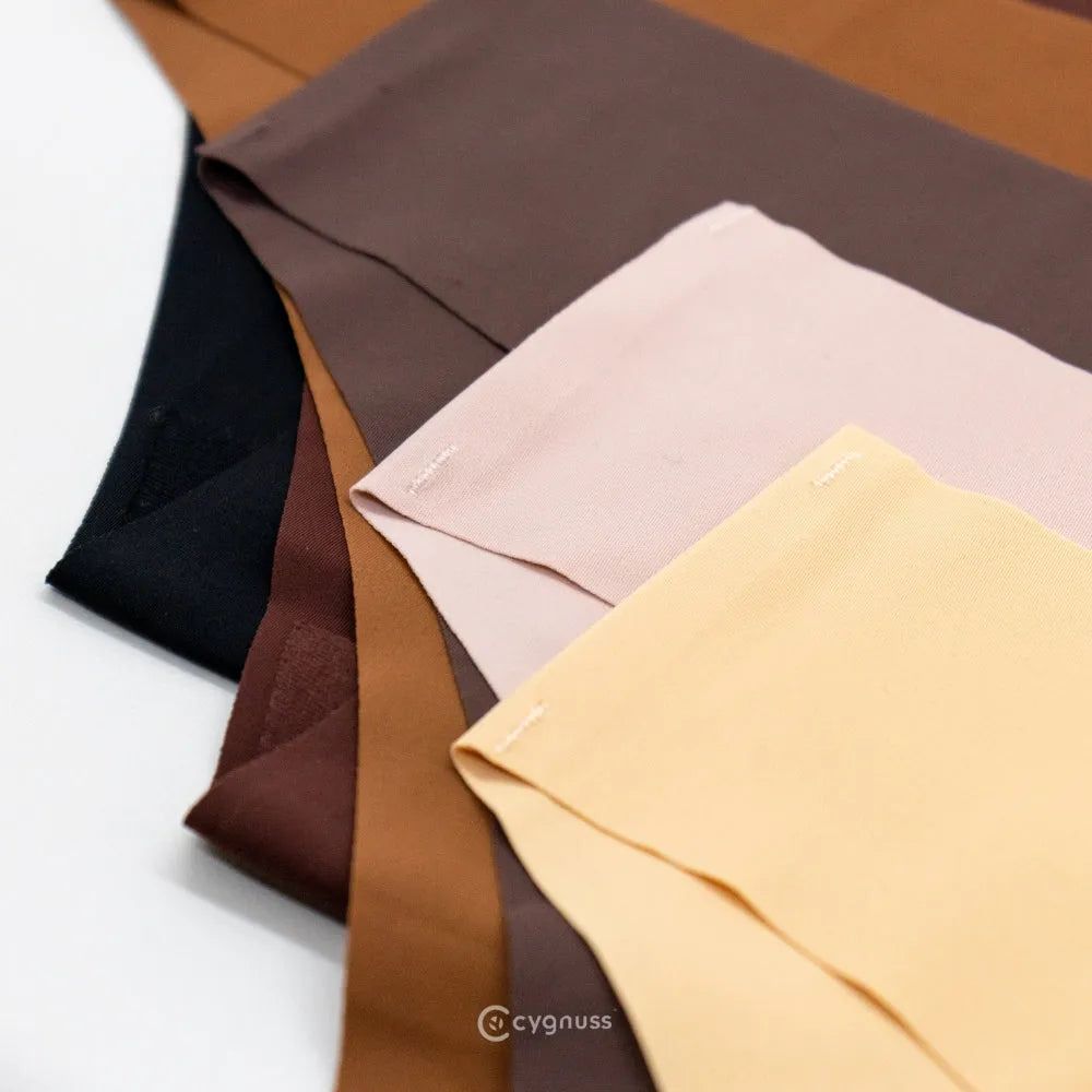 Imagem de calcinhas sem costura da Cygnuss em tons neutros, incluindo preto, marrom, bege e rosa claro, dispostas sobre uma superfície clara. O foco está nos detalhes do acabamento, destacando a qualidade do corte e a costura reforçada.