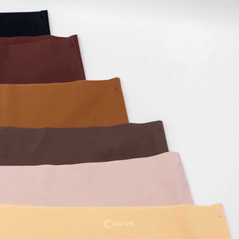 Imagem de calcinhas sem costura da Cygnuss organizadas em degradê de tons neutros, incluindo preto, marrom, caramelo, rosa claro e bege. O design minimalista e o acabamento preciso destacam a qualidade das peças