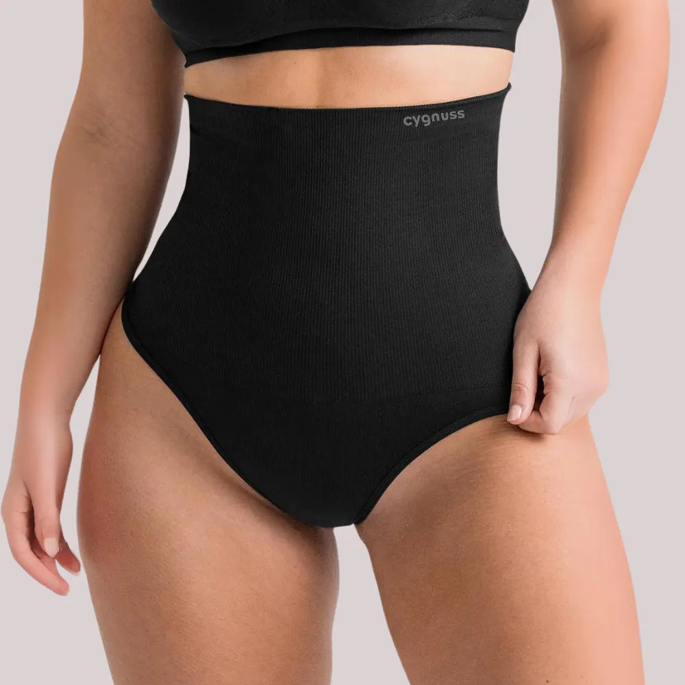 Mulher vestindo a Calcinha Modeladora Pêra da Cygnuss, modelo tanga na cor preta, com cintura super alta e tecido compressivo, destacando a modelagem do abdômen e o caimento firme no corpo.