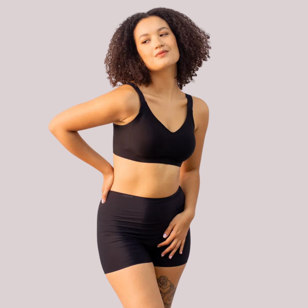 Imagem de uma mulher usando o Conjunto Short Segunda Pele Sem Costura e o sutiã sem costura na cor preta. O conjunto oferece conforto e modelagem discreta, ideal para o dia a dia, sem deixar marcas ou costuras visíveis.