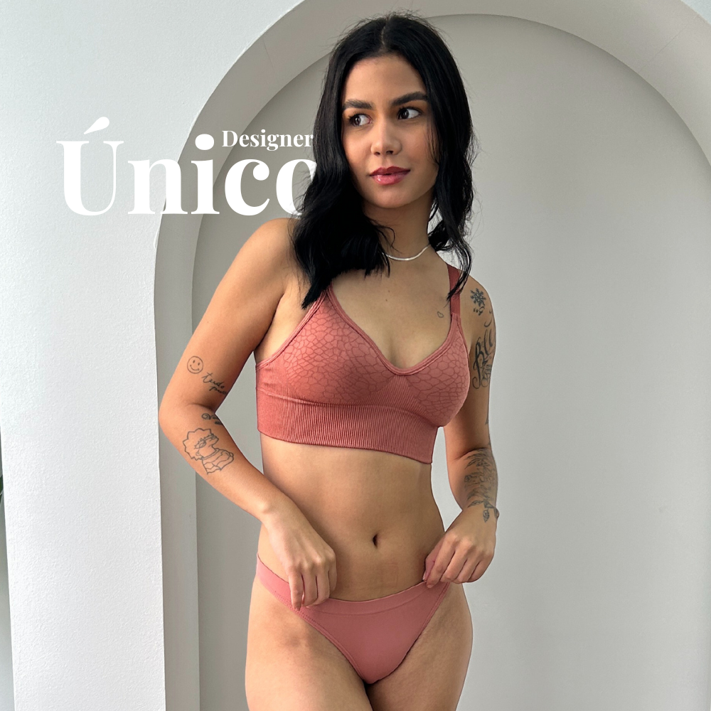 Mulher usando o conjunto da linha Trend Curves Cygnuss x Lupo na cor terracota, composto por sutiã sem aro com textura em relevo e calcinha básica, em ambiente claro com a palavra “Único” ao fundo.