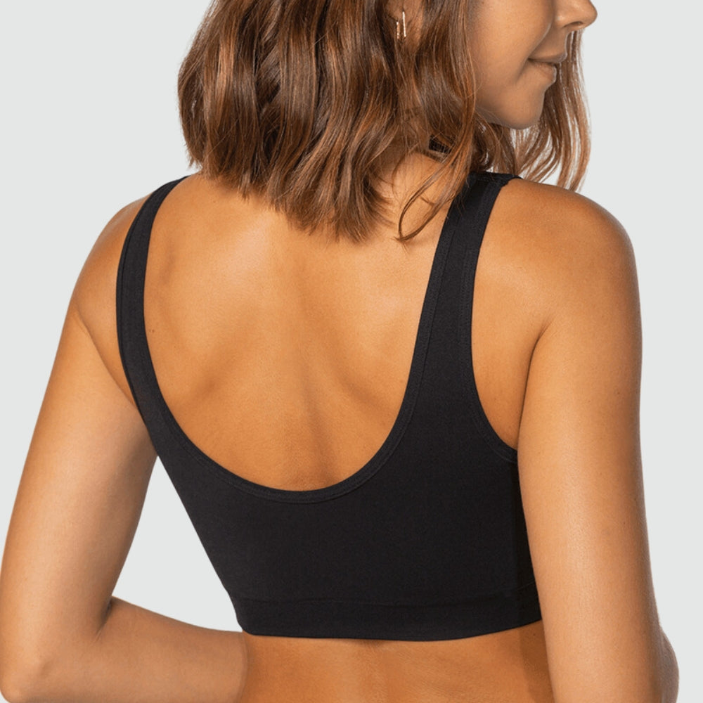 Imagem mostra as costas de uma mulher usando top preto sem costura da Cygnuss em parceria com a Lupo. O modelo possui alças largas e decote profundo nas costas, oferecendo liberdade de movimento e conforto. O fundo cinza claro mantém o foco na peça.