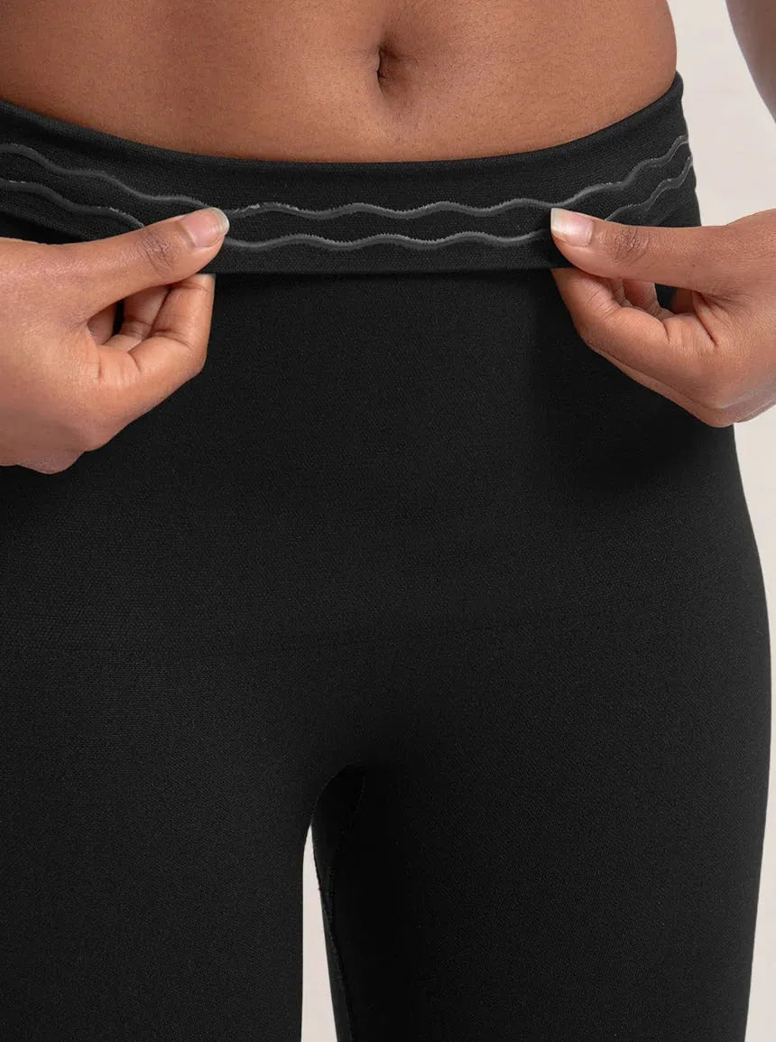 Close-up da Legging Jade Fit Modeladora de Cós Alto na cor preta, com foco no cós sendo levemente puxado para mostrar o detalhe interno em silicone antiderrapante que ajuda a manter a peça no lugar durante o uso.