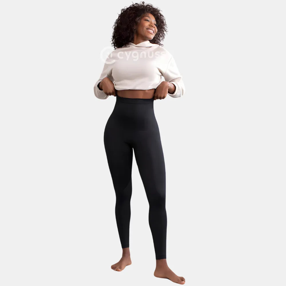 Mulher sorridente usando a Legging Jade Fit Modeladora de Cós Alto na cor preta, combinada com moletom cropped bege, em pose leve e descontraída que destaca o cós alto e o ajuste anatômico da peça.