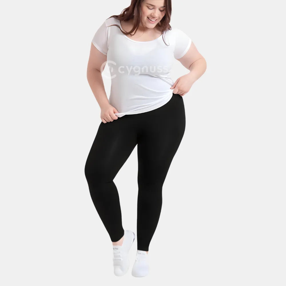 Mulher plus size sorridente usando a Legging Jade Fit Modeladora de Cós Alto na cor preta, combinada com camiseta branca e tênis, em pose descontraída que evidencia a versatilidade e conforto da peça para o dia a dia.