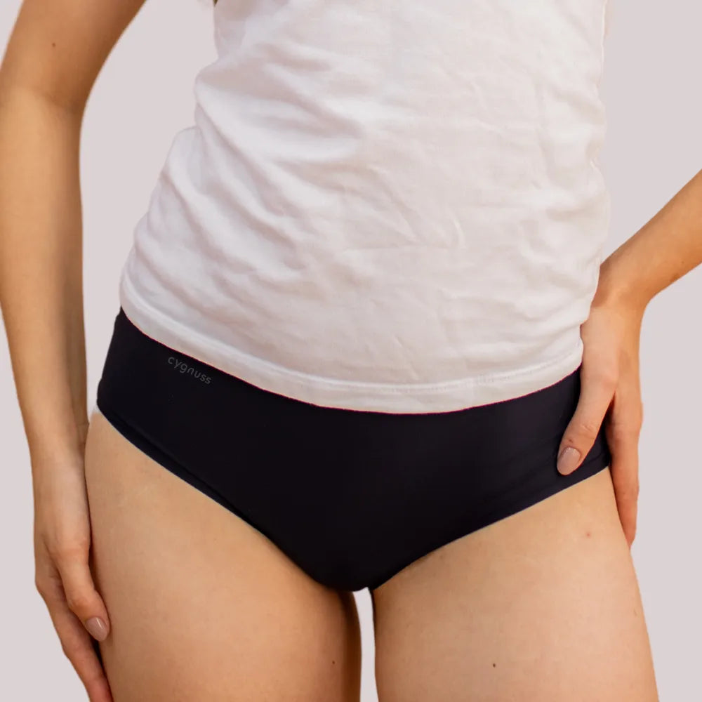 Mulher vestindo uma camiseta branca e uma calcinha preta sem costura da Cygnuss. A imagem destaca o ajuste confortável da peça e seu design discreto, ideal para o dia a dia.
