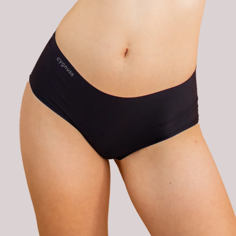 Imagem em close da região do quadril de uma mulher usando uma calcinha preta da Cygnuss. O modelo sem costura proporciona um ajuste confortável e discreto.