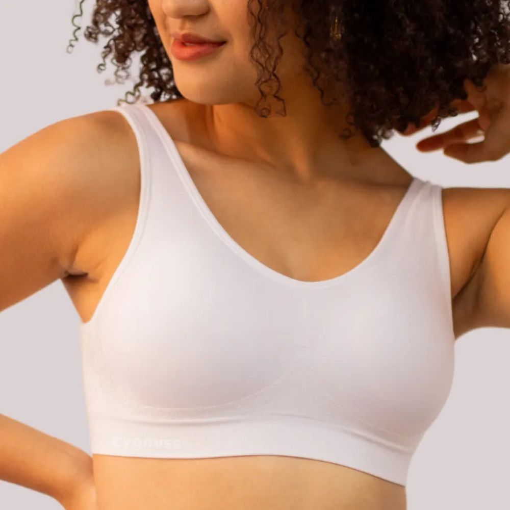 Mulher usando o Sutiã Daily Original na cor branca, sorrindo e levantando o braço, destacando o ajuste confortável, as alças largas e o design sem costura para suporte ideal.