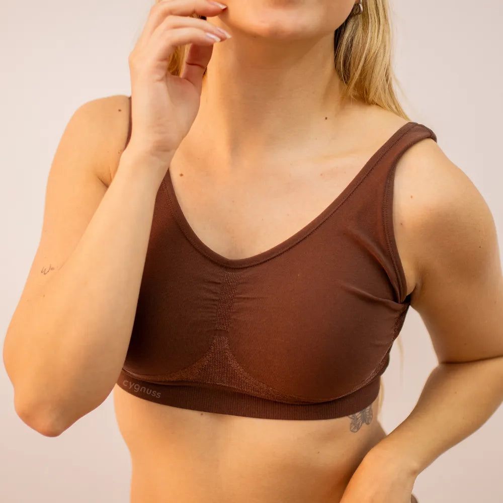 Mulher usando o Sutiã Daily Original na cor marrom, posando com a mão próxima ao rosto. O modelo sem costura oferece conforto, sustentação e um ajuste anatômico perfeito.