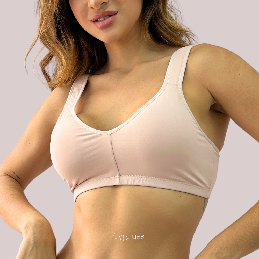 Mulher vestindo o Sutiã Daily Original na cor rosé da Cygnuss. O modelo sem costuras se ajusta ao corpo com suavidade, proporcionando conforto e sustentação. A alça larga e o tecido de toque macio destacam o design minimalista e sofisticado da peça.