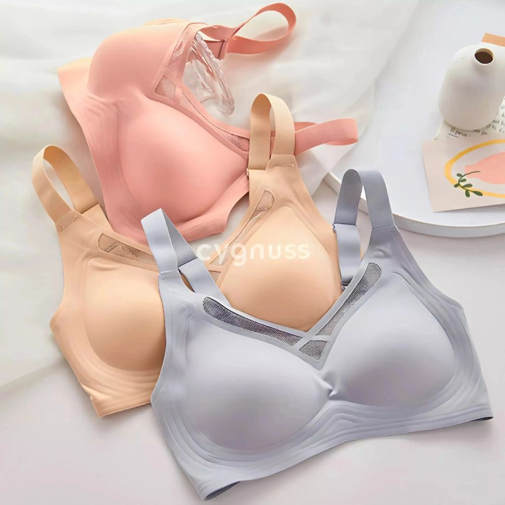 Três unidades do Sutiã Dreams da Cygnuss em diferentes cores – cinza, nude e rosé – dispostas sobre uma superfície branca, ao lado de uma xícara e um vaso decorativo. O design sem costuras e os detalhes em tule no decote são evidenciados, destacando o conforto e sofisticação da peça.