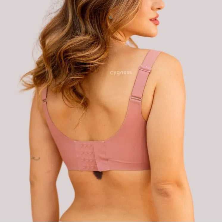 Mulher de costas vestindo o Sutiã Dreams na cor rosa, destacando o fecho ajustável com quatro níveis de regulagem e as alças largas para maior sustentação e conforto. O tecido sem costuras proporciona um ajuste suave ao corpo. O cabelo da modelo está solto e ondulado, e o fundo da imagem é em tom neutro.