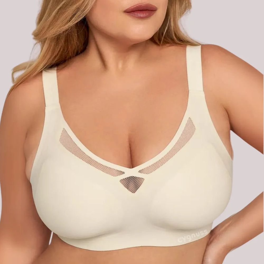 Mulher plus size vestindo o Sutiã Dreams na cor bege, destacando o design sem costuras, com detalhes vazados em tule no decote e alças largas para maior sustentação e conforto. O logo da Cygnuss está visível na parte inferior do sutiã.