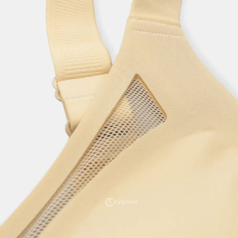 Close-up do Sutiã Dreams na cor nude, destacando os detalhes vazados em tule na lateral e a costura reforçada das alças ajustáveis. O tecido sem costuras e o design ergonômico proporcionam conforto e sustentação. O logo da Cygnuss está visível na parte inferior da peça.