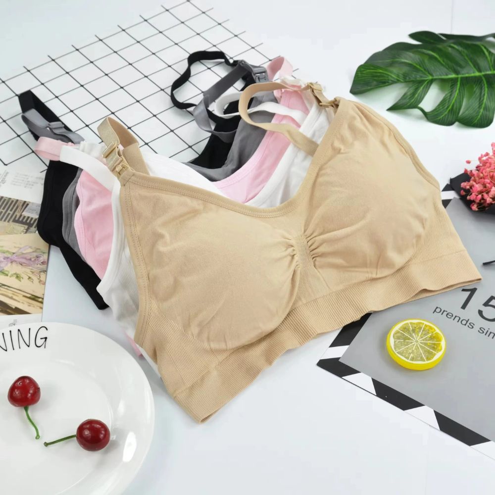 Conjunto de cinco Sutiãs Amamentação sem Bojo da collab Cygnuss x Lupo organizados sobre uma superfície decorada. As cores visíveis incluem bege, branco, rosa claro, cinza e preto. As peças possuem alças com clipes para amamentação e franzido central para ajuste anatômico.