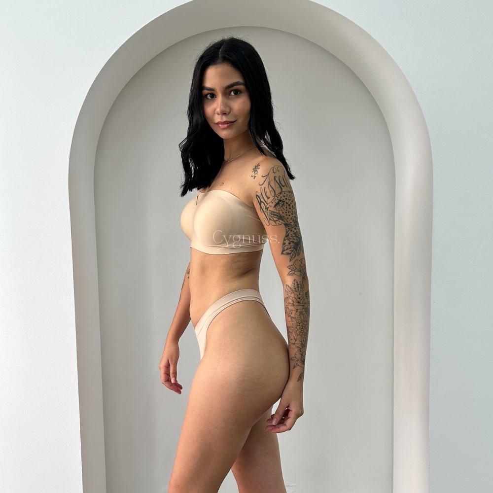 Modelo posando de perfil vestindo o Sutiã Tomara que Caia Sensação na cor bege. A peça destaca o caimento perfeito, sustentação firme sem alças e design minimalista que valoriza as curvas naturais do corpo