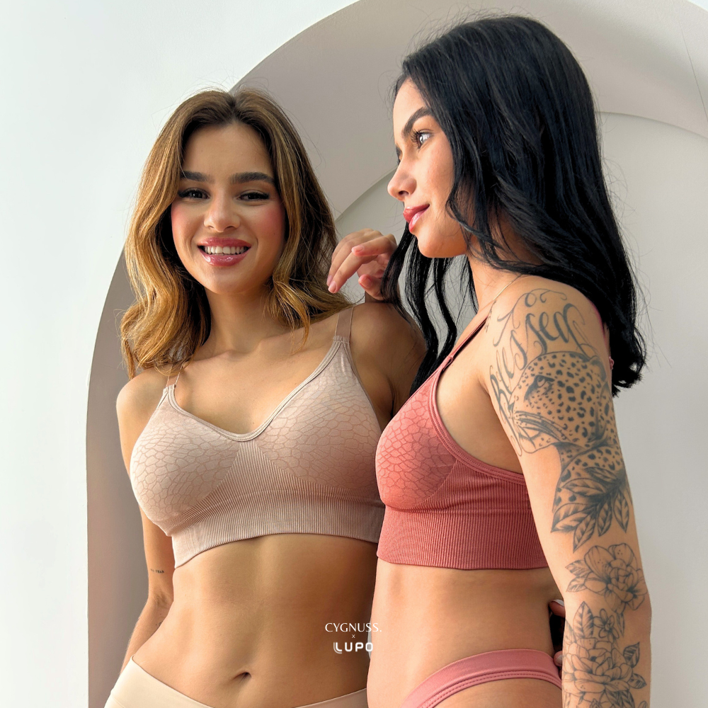 Duas mulheres usando o Sutiã Trend Curves Cygnuss x Lupo, uma na cor bege e a outra na cor terracota, sorrindo e interagindo em um ambiente claro, destacando o caimento natural, conforto e estilo da peça.