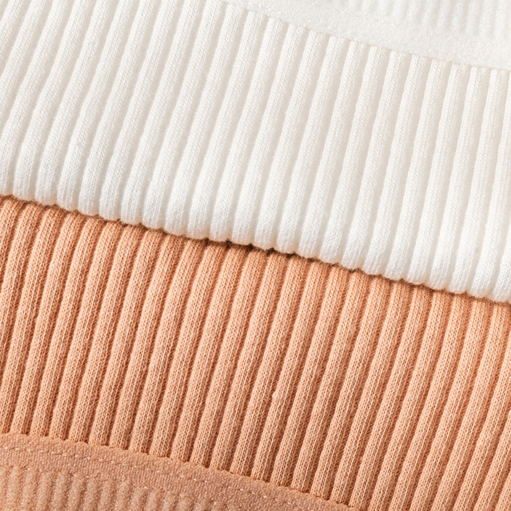 Close em tecidos canelados de calcinhas empilhadas, nas cores branca, terracota e bege claro. A imagem destaca a textura do tecido e o acabamento das costuras, transmitindo a maciez e qualidade do material.