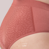 Close-up lateral de uma mulher usando uma calcinha modeladora de cintura alta na cor telha. O tecido possui um padrão texturizado elegante e sem costuras, oferecendo compressão moderada e conforto. A modelagem firme ajusta-se ao corpo, proporcionando definição e sustentação. O logotipo da Cygnuss & Lupo está sobreposto na parte inferior da peça. Fundo nude rosado.