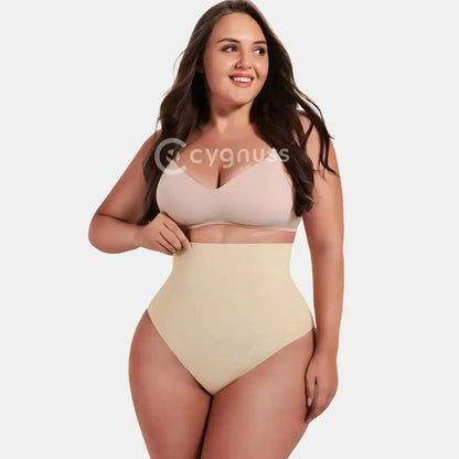 Mulher vestindo a Calcinha Modeladora Pêra da Cygnuss, modelo tanga na cor bege, com cintura alta e efeito modelador na região abdominal, sorrindo e posando com top nude em fundo claro.
