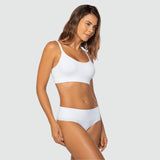 Modelo usando conjunto branco da Cygnuss + Lupo, com top de alças finas e calcinha cintura alta. Ela posa de frente em posição lateral, destacando a modelagem anatômica e o conforto das peças.