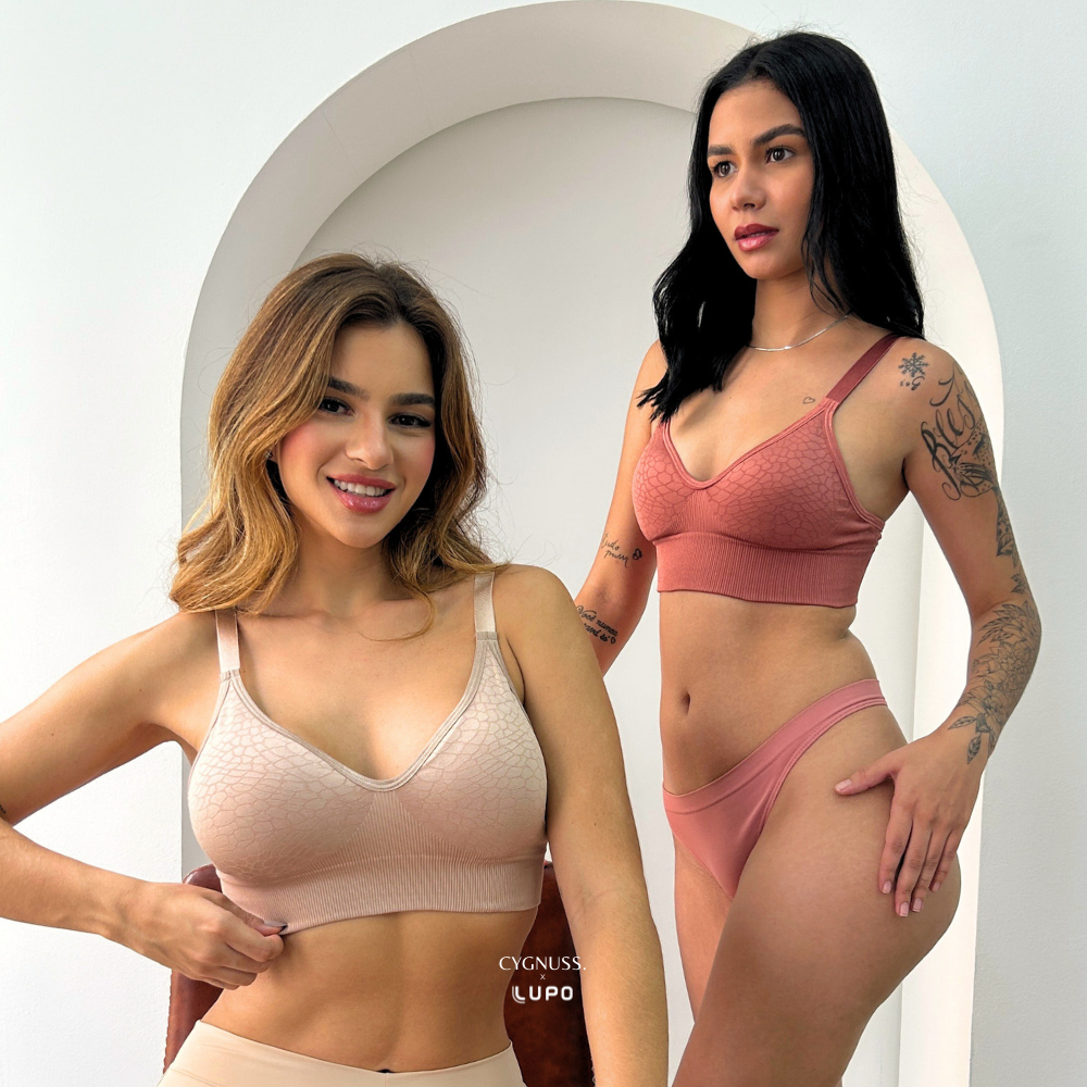 Duas mulheres usando os conjuntos Trend Curves Cygnuss x Lupo, uma na cor bege e a outra na cor terracota, em ambiente claro com arco decorativo, exibindo o sutiã com textura em relevo e calcinhas combinando.
