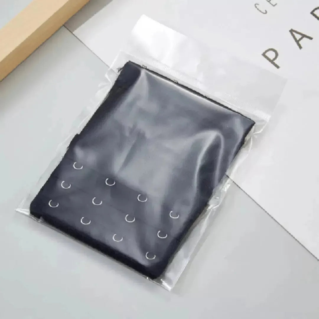 Extensor de sutia preto com tres niveis de ajuste, embalado individualmente em plastico transparente. Ideal para oferecer praticidade, higiene e maior conforto ao adaptar o sutia ao corpo. Fundo claro com detalhes minimalistas.