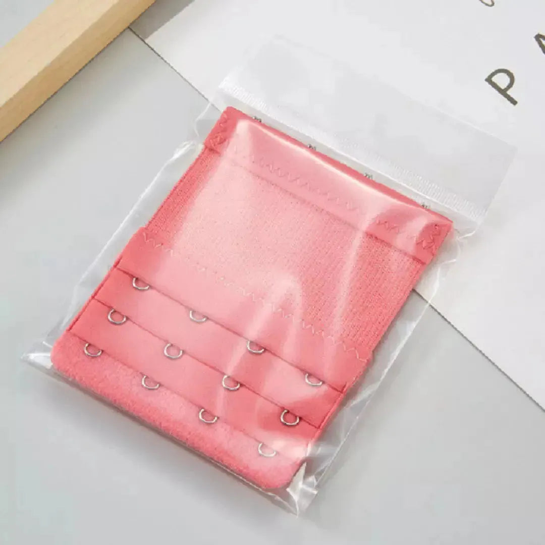 Extensor de sutia rosa escuro com tres niveis de ajuste e ganchos reforcados, embalado individualmente em plastico transparente. Ideal para proporcionar mais conforto e flexibilidade no uso do sutia. Fundo claro com organizacao minimalista.