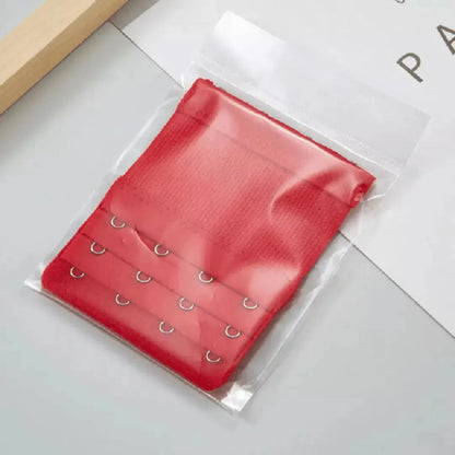 Extensor de sutia vermelho com tres niveis de ajuste e ganchos metalicos, embalado individualmente em plastico transparente. Ideal para ajustar o sutia com mais conforto e prolongar seu uso. Fundo claro com visual limpo.