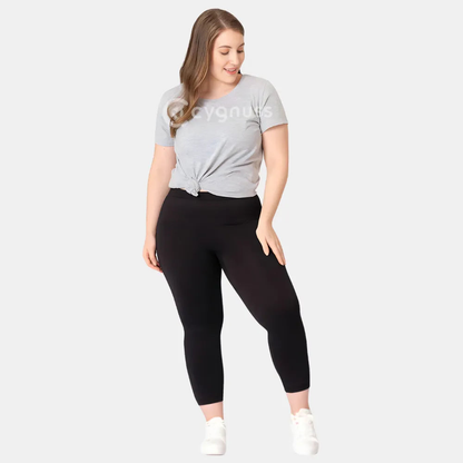 Mulher plus size usando a Legging Jade Fit Modeladora de Cós Alto na cor preta, combinada com camiseta cinza amarrada e tênis branco, em pose descontraída que evidencia o conforto e a versatilidade da peça no dia a dia.

